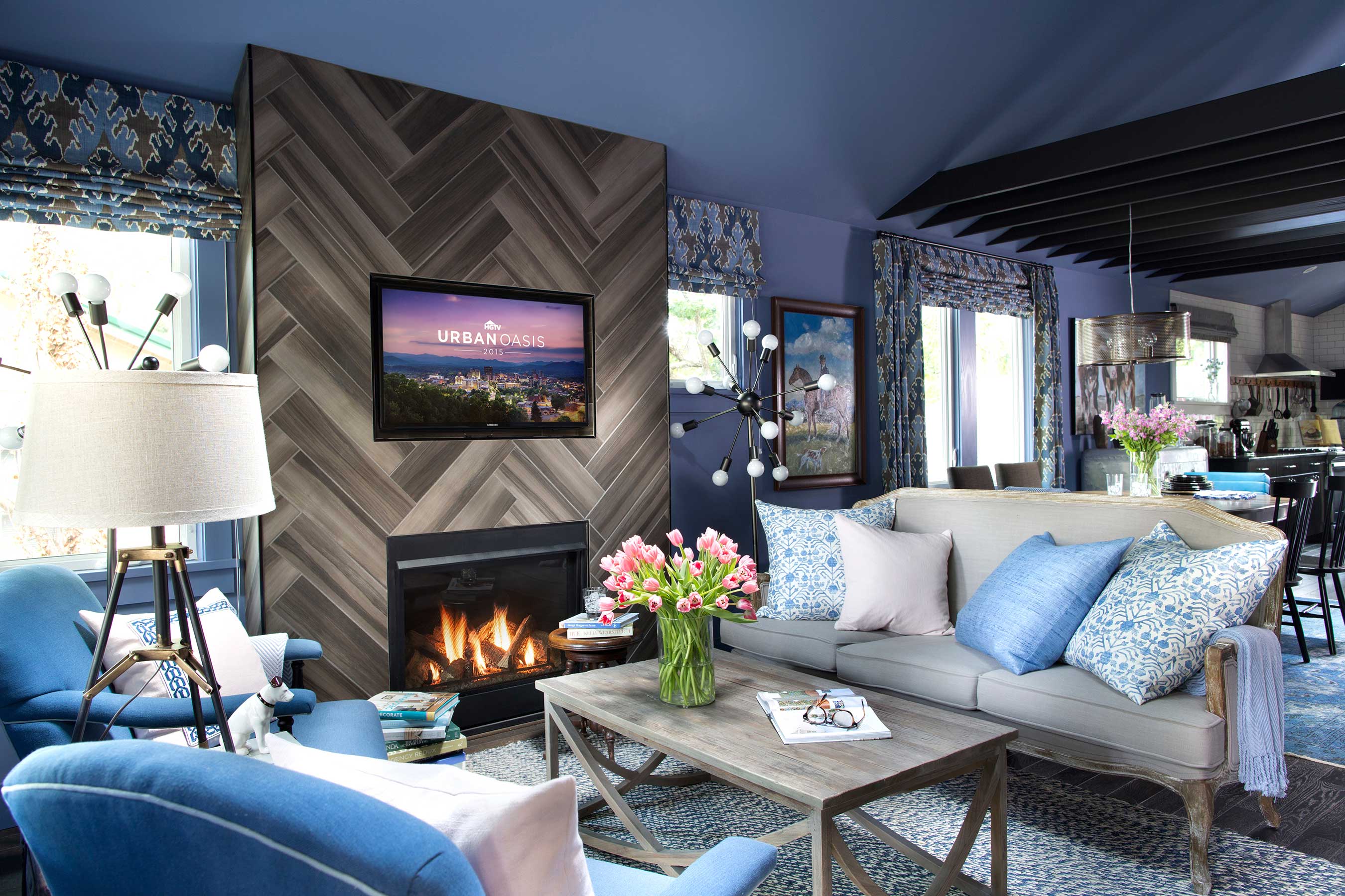 Inside the front door of the HGTV Urban Oasis, the dramatic blue-gray walls and comfortable seating are centered around a ceiling-high fireplace set in a beautiful herringbone-patterned tile.