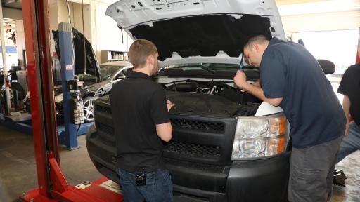 A professional mechanic inspects the engine as the owner looks on