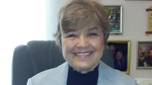 Portrait of Barbara Borrell, cancer survivor, sitting in an office chair, smiling.