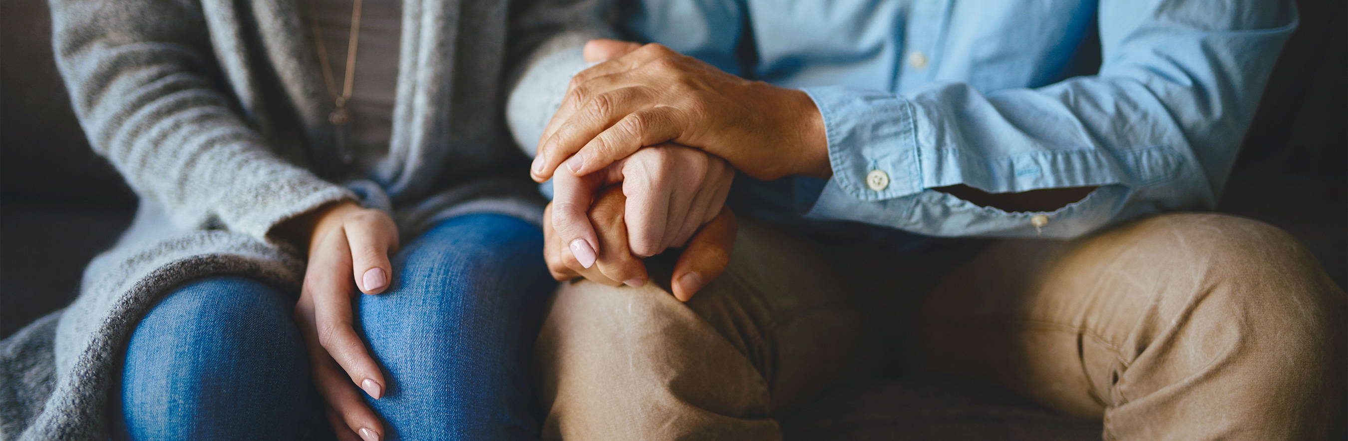 Woman and man sitting next to each other holding hands.