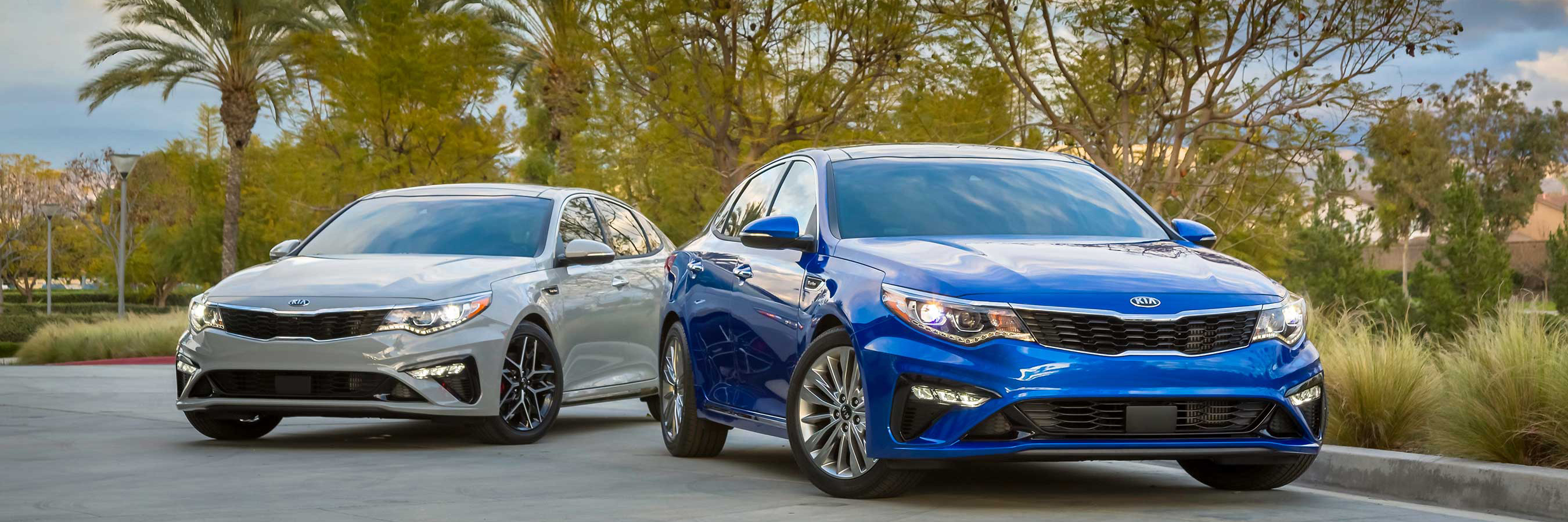 A blue Kia Optima and a silver Kia Optima parked beside one another.