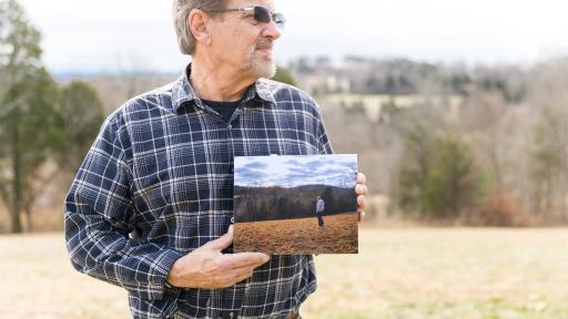 Mr. Wood holding a photo of a man standing in the same field as he currently is