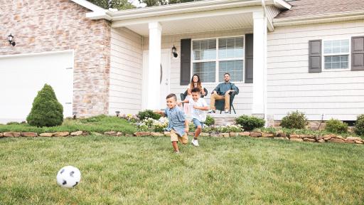 Wife and Husband sit on porch while watching their children play soccer on the grass
