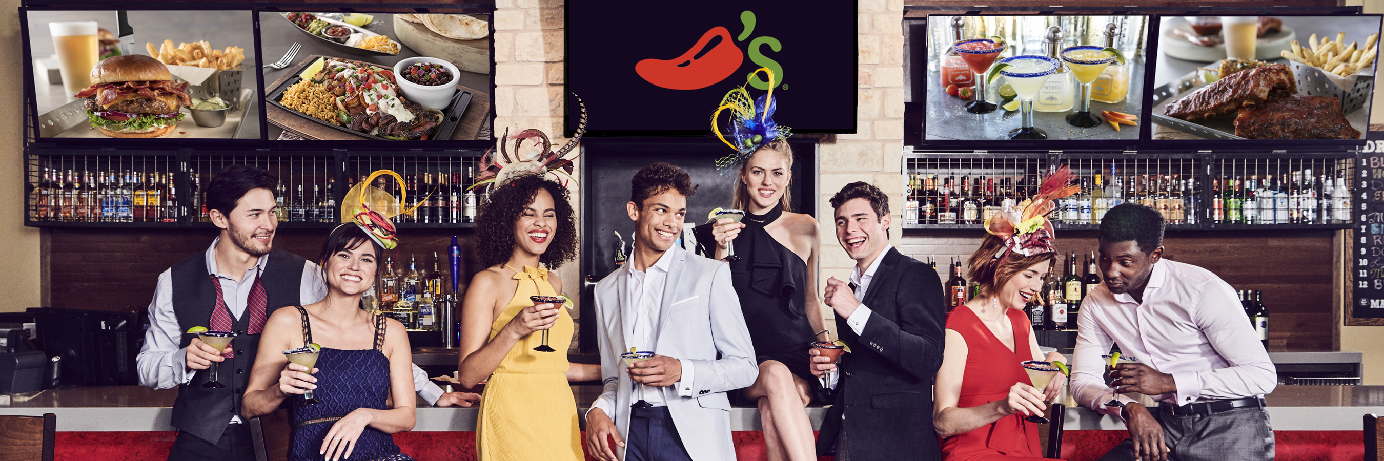 Fancily-clad men and women sit and stand around a bar counter, behind them the Chili&rsquo;s logo.