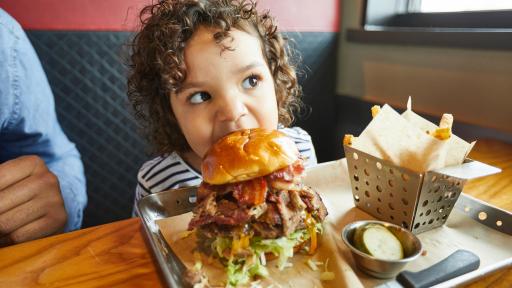 Young child taking a bite of a very large burger