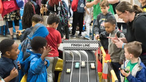 Children watching toy cars race down a track towards the finish line
