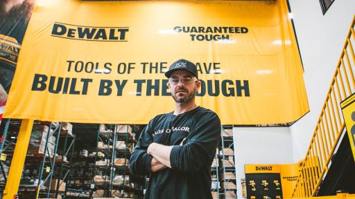 Brian Steorts standing with arms crossed beneath a large yellow banner. The banner has the DeWalt logo, a guarantee of toughness, and the slogan, "Tools of the brave, built by the tough."