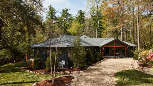 A ranch with stone driveway, all surrounded by trees.