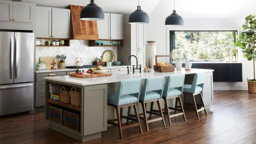 A modern kitchen with hanging lights, decorative island lined with chairs, and wood floor.