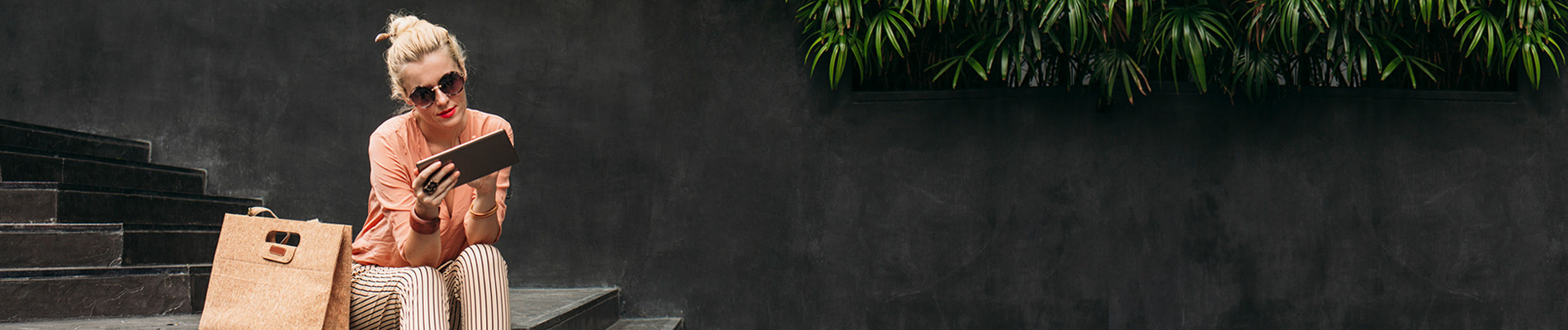 Blonde woman wearing sunglasses looking at her tablet.