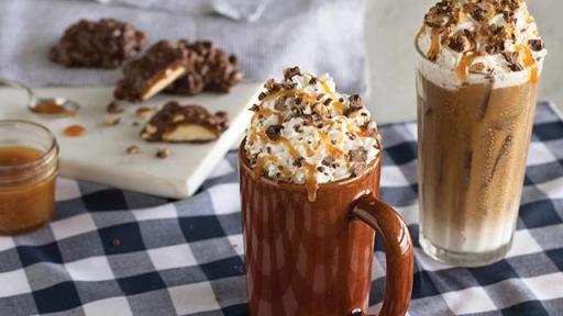 Two latte drinks with whip cream, caramel and chocolate toppings