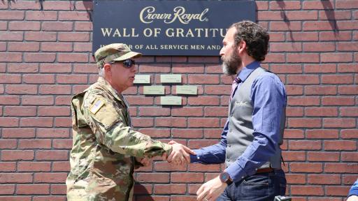Solider and man shaking hands in front of appreciation wall