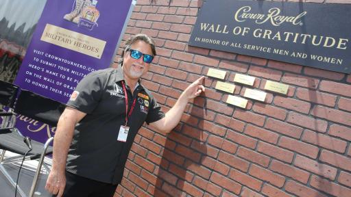 Man with dark grey shirt and sunglasses pointing to plaque on Wall of Gratitude