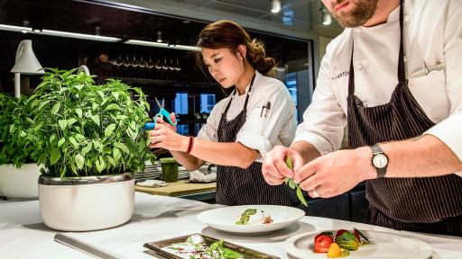 Two chefs preparing plates of food with basil.