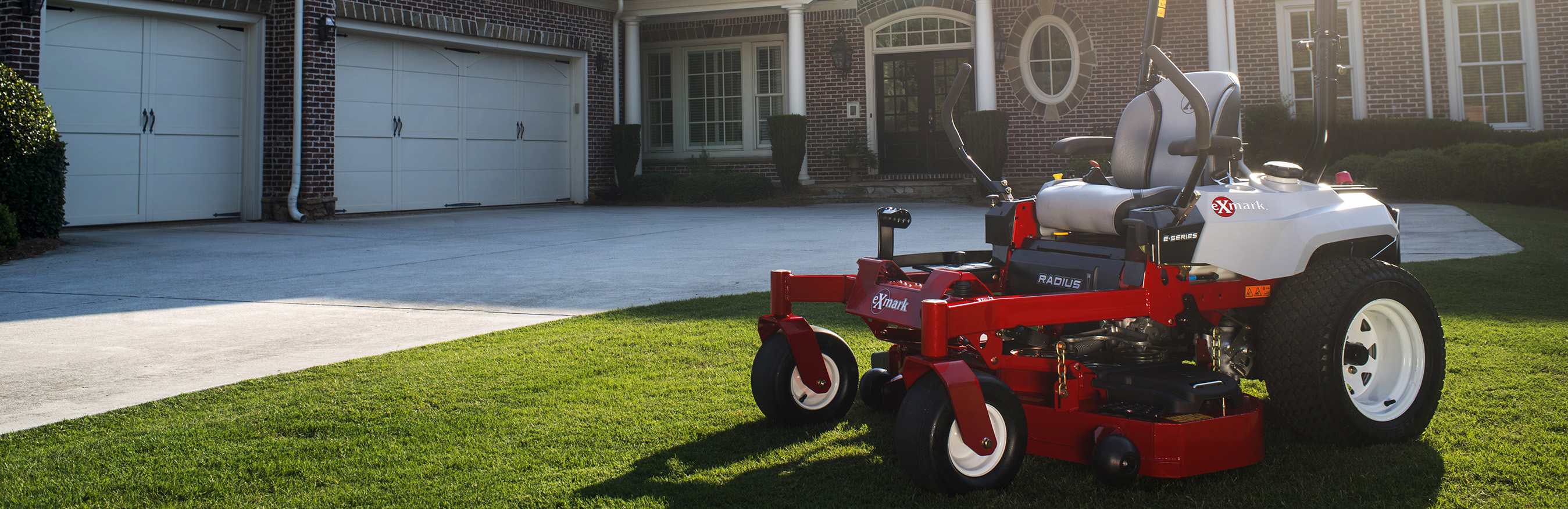 Red Exmark lawn mower parked on grass in yard of large brick house