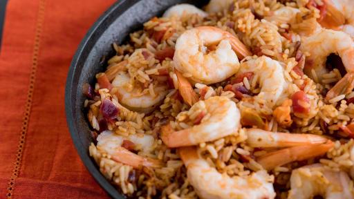 A black bowl on a red tablecloth with seasoned rice and shrimp.