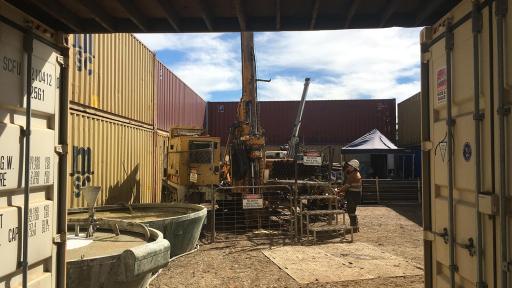 Man working a large piece of machinery surrounded by shipping containers