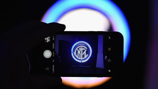 A hand holding a phone in a dark room. A light shines from the background that is blurred, but shows up clearly on the phone to depict a symbol.