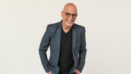 Howie Mandel with glasses standing in a suit
