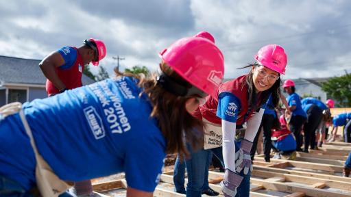 Women helping each other on frame of house