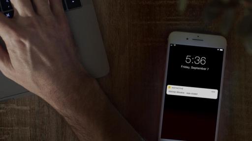 Person working at computer desk with iPhone close by on desk displaying a notification from the Pella Insynctive App