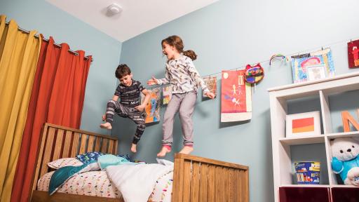 Kids jumping on bed with First Alert Onelink Safe & Sound product on ceiling.