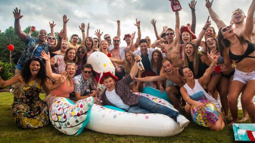 Man on a giant inflatable swan surrounded by friends at a pool party.