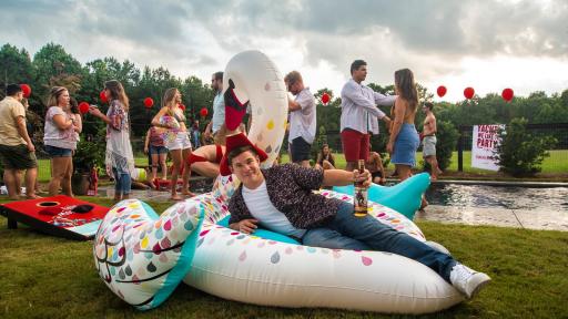 Man at a pool party lying on an inflatable swan with a bottle of captain morgan