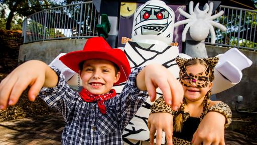 Boy dressed up as a cowboy and girl dressed up as a leopard standing in front of a Lego mummy
