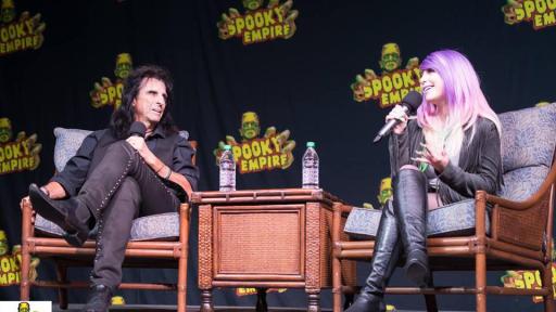 Alice Cooper on stage conversing with a woman with purple hair.