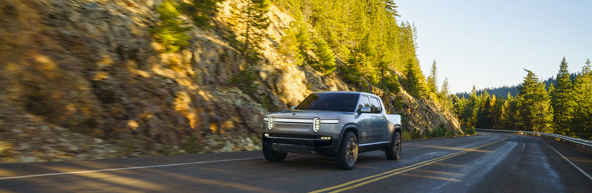 Rivian Automotive all-electric pickup R1T driving down a wooded road.