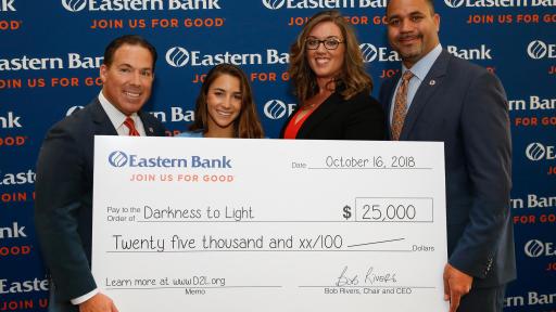 Bob Rivers (left), Chair & CEO of Eastern Bank, and Quincy Miller (right), Vice Chair & President of Eastern Bank, present Aly Raisman and Katelyn Brewer with a donation for $25,000 to Darkness to Light.