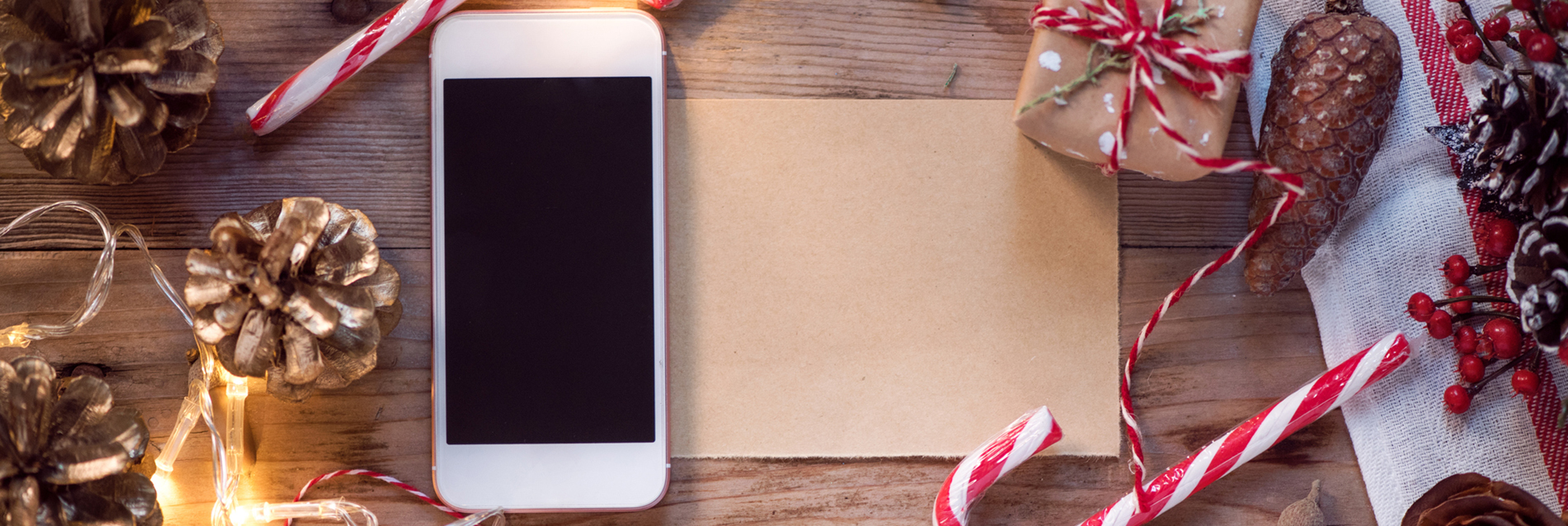 Phone laid atop paper, surrounded by various Christmas trinkets: candy canes, bows, pine cones, bows, and holly.
