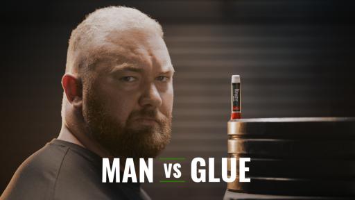 A very tough looking Hafthor Bjornsson looks at the camera with a stick of Krazy Glue on some weights beside him, the banner says Man vs. Glue.