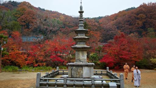 Three Buddhist monks circling a stone stupa.