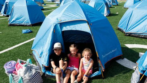 Three young children sitting in the front door of their blue tent.