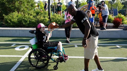 A man hands a football to a child in a wheelchair.