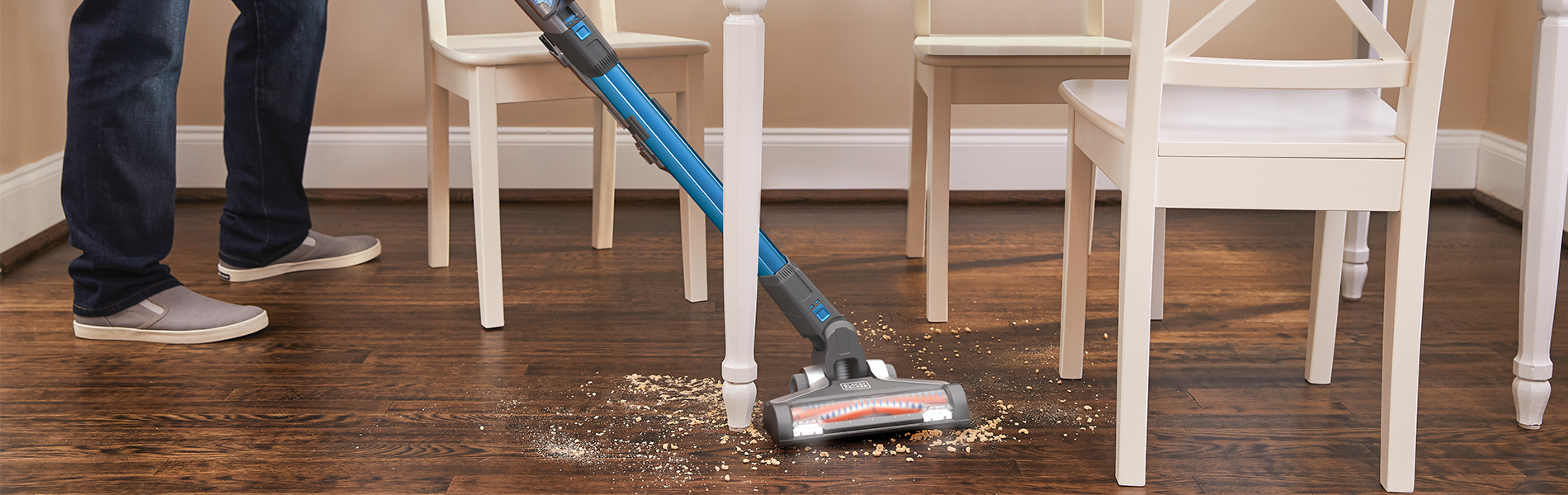 Cordless vacuum sweeping between a kitchen table and chairs.