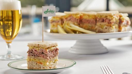 Sadelle's Turkey and Roast Beef Triple Decker Sandwich on a cake platter on a white tablecloth