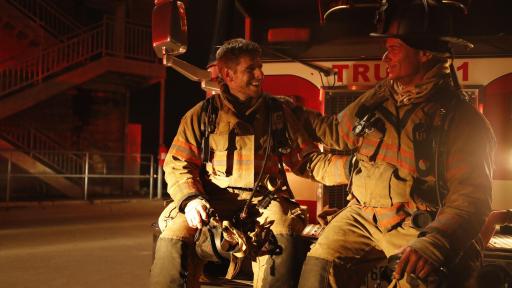 Firemen sitting on the front of their firetruck at night.