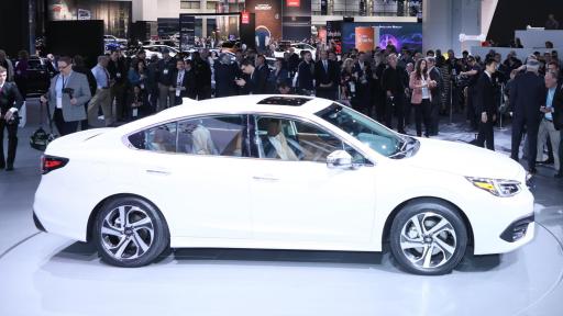 Side profile of a white 2020 Subaru Legacy surrounded by people and photographers.