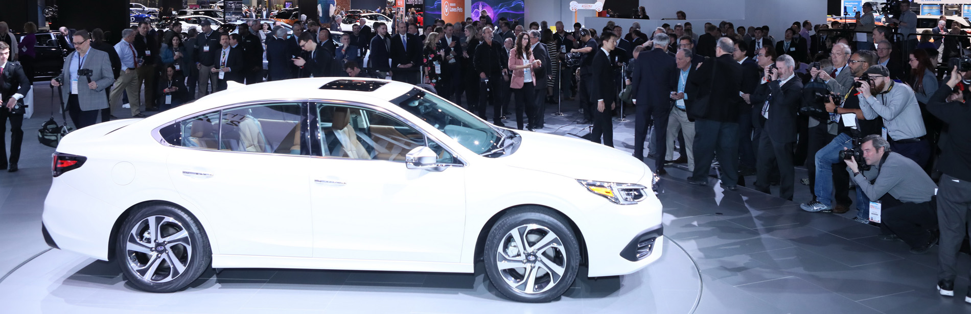 A white 2020 Subaru Legacy surrounded by a crowd and photographers.