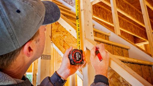 A worker using a tape measurer on a beam