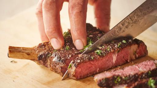 Closeup of a hand cutting a steak.