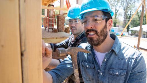 Two men working on nailing screws into posts within house.