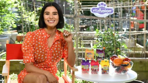 Actress Diane Guerrero Joins vitafusion™ sits on a chair by a table with vitafusion products
