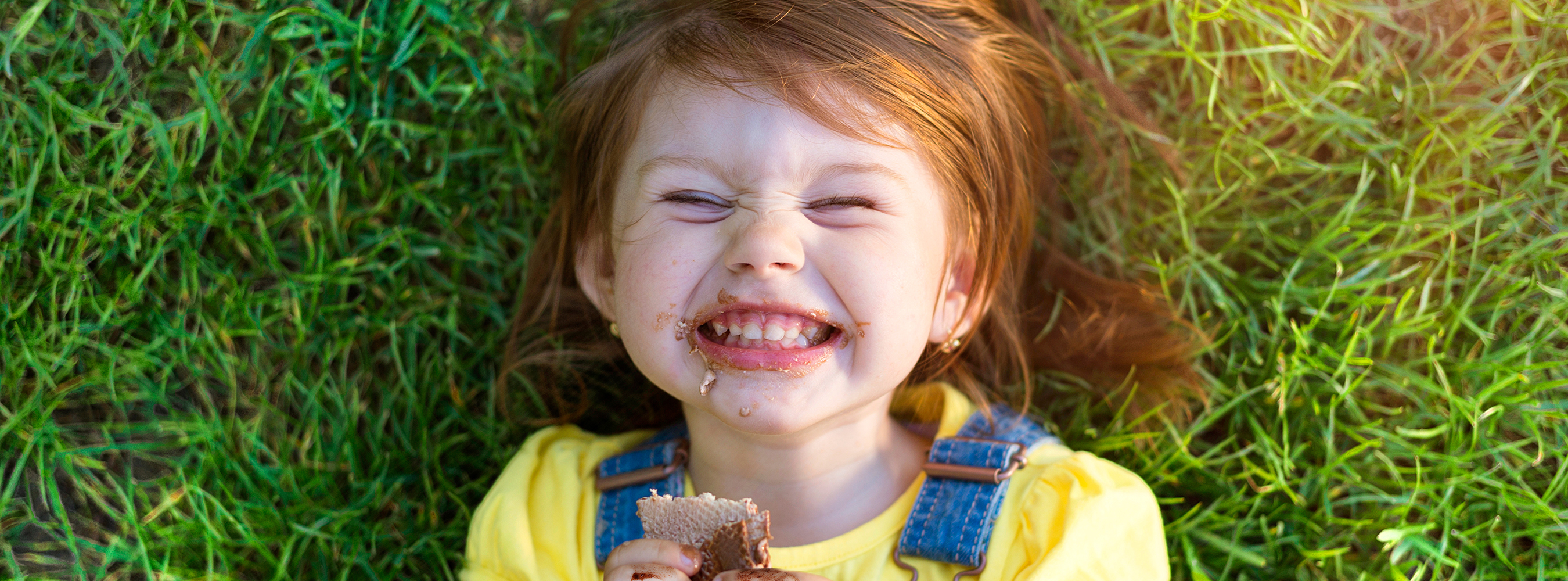 Banner image of a young girl smiling and messy from eating a chocolate bar