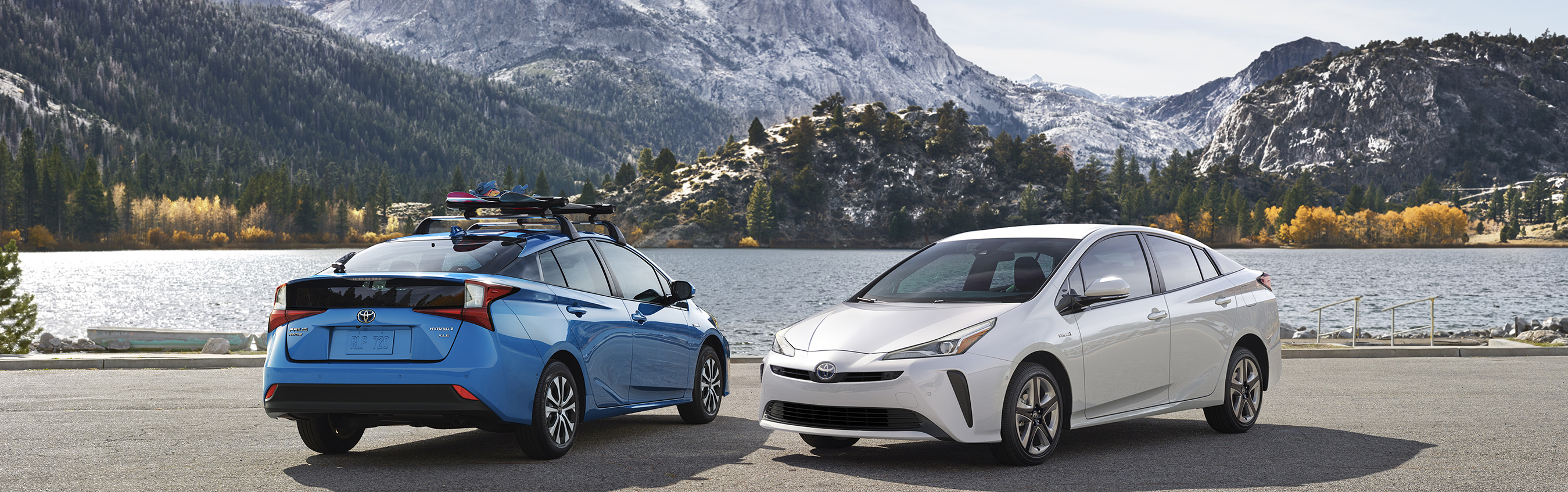 Two cars parked near one another by a lake with mountains in the backdrop
