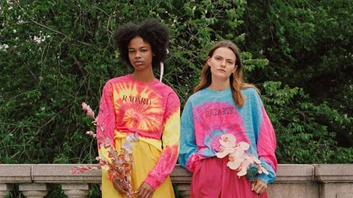 Two models holding flower wearing brightly colored tye-dye shirts