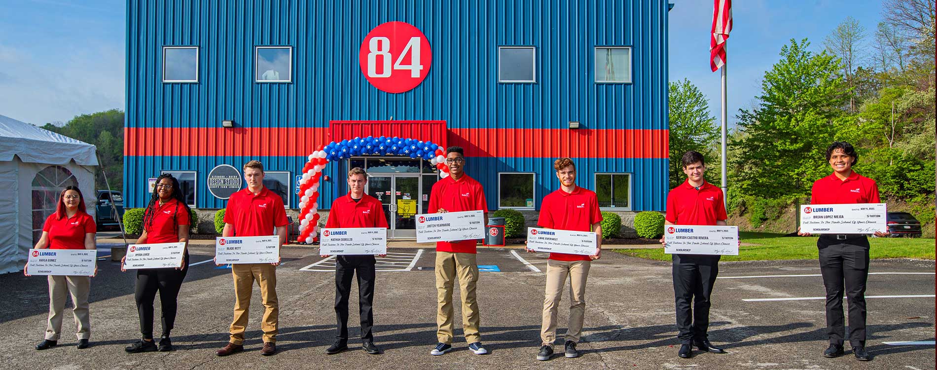 scholarship winners in orange shirts lined up in front of 84 building